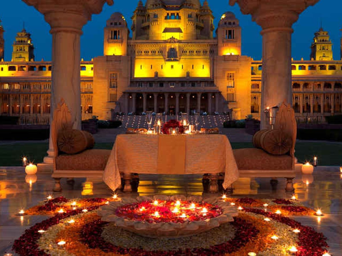 Romantic candle lit dinner setup with flower decorations in front of the illuminated Udaipur City Palace in Rajasthan ideal for a luxurious honeymoon destination in India